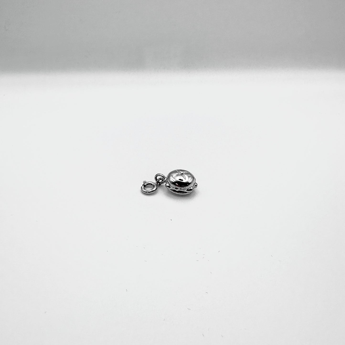 Ein kleiner, silberner Anhänger in Form von „Drei im Weggla“ liegt auf einer weißen Oberfläche. Das detailreiche Schmuckstück zeigt ein klassisches fränkisches Brötchen mit drei Bratwürsten und ist mit einem Verschluss versehen, sodass es leicht an einer Kette oder einem Armband befestigt werden kann. Die glänzende Oberfläche betont die hochwertige Verarbeitung des Designs.