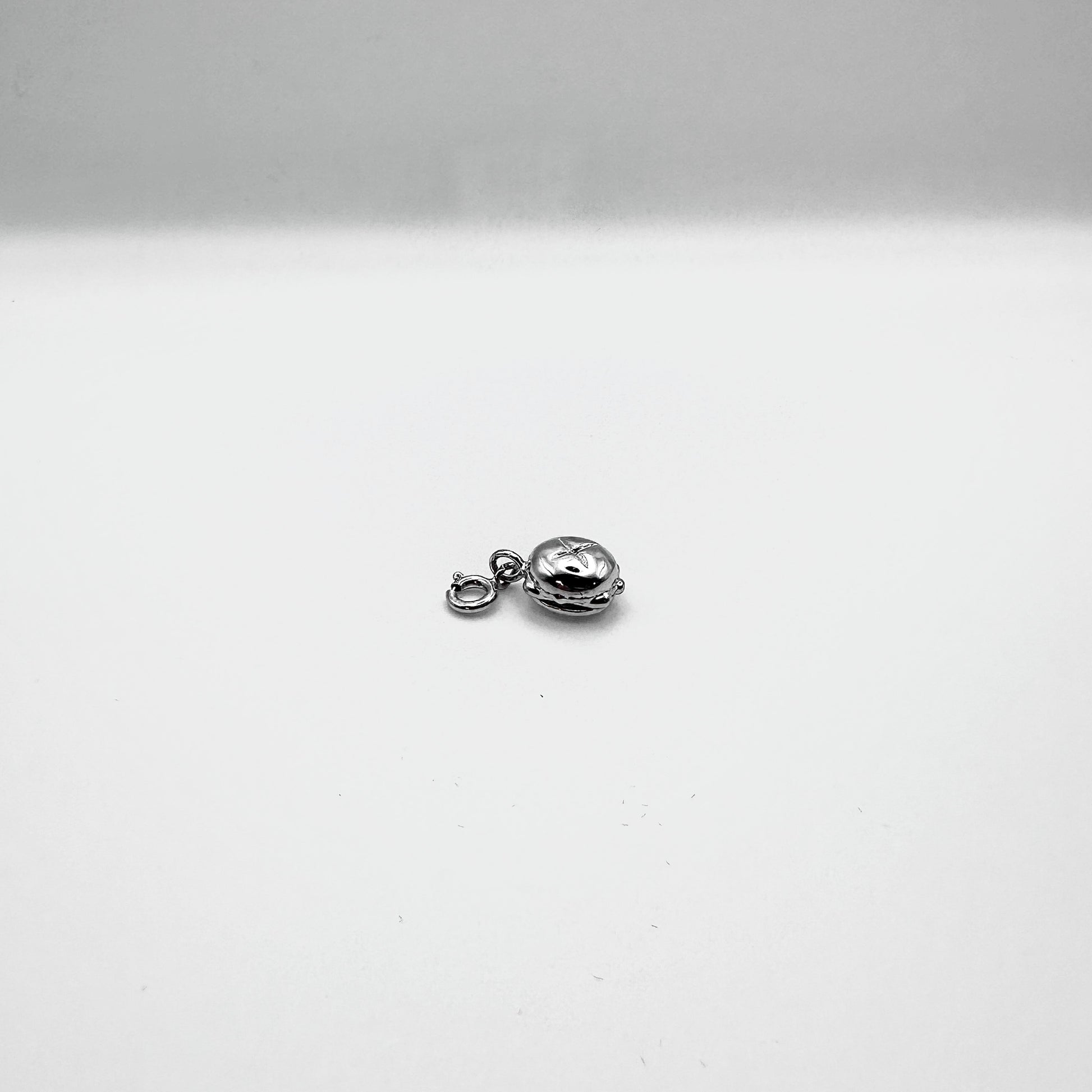 Ein kleiner, silberner Anhänger in Form von „Drei im Weggla“ liegt auf einer weißen Oberfläche. Das detailreiche Schmuckstück zeigt ein klassisches fränkisches Brötchen mit drei Bratwürsten und ist mit einem Verschluss versehen, sodass es leicht an einer Kette oder einem Armband befestigt werden kann. Die glänzende Oberfläche betont die hochwertige Verarbeitung des Designs.