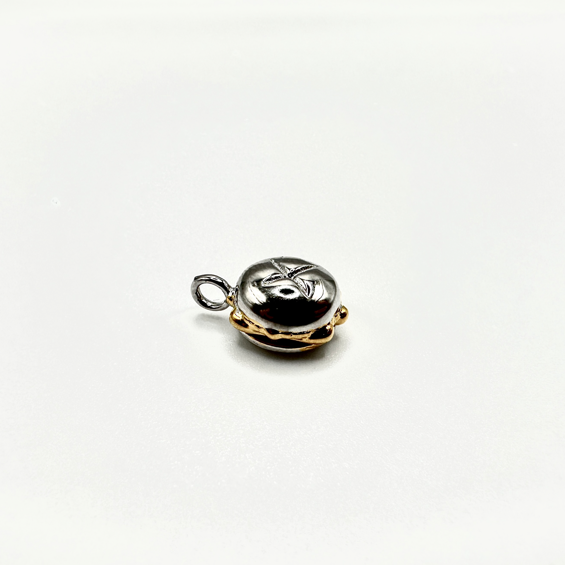 Edler Anhänger in Form des traditionellen „3 im Weggla“ – einem Nürnberger Bratwurstbrötchen. Die detailreiche Miniatur ist aus einer Kombination von Silber und Vergoldung gefertigt, wobei das glänzende Silber die Oberfläche des Brötchens darstellt und die goldfarbenen Akzente die Wurst und die unteren Partien hervorheben. Der Anhänger liegt auf einem schlichten weißen Hintergrund und verfügt über eine kleine Öse zur Befestigung an einer Kette oder einem Armband.