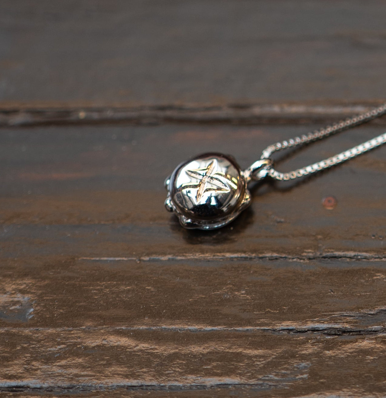 Silberne Halskette mit einem Anhänger in Form von „3 im Weggla“, kunstvoll gestaltet mit feinen Details und einem Sternmotiv, liegend auf einer rustikalen Holzoberfläche.