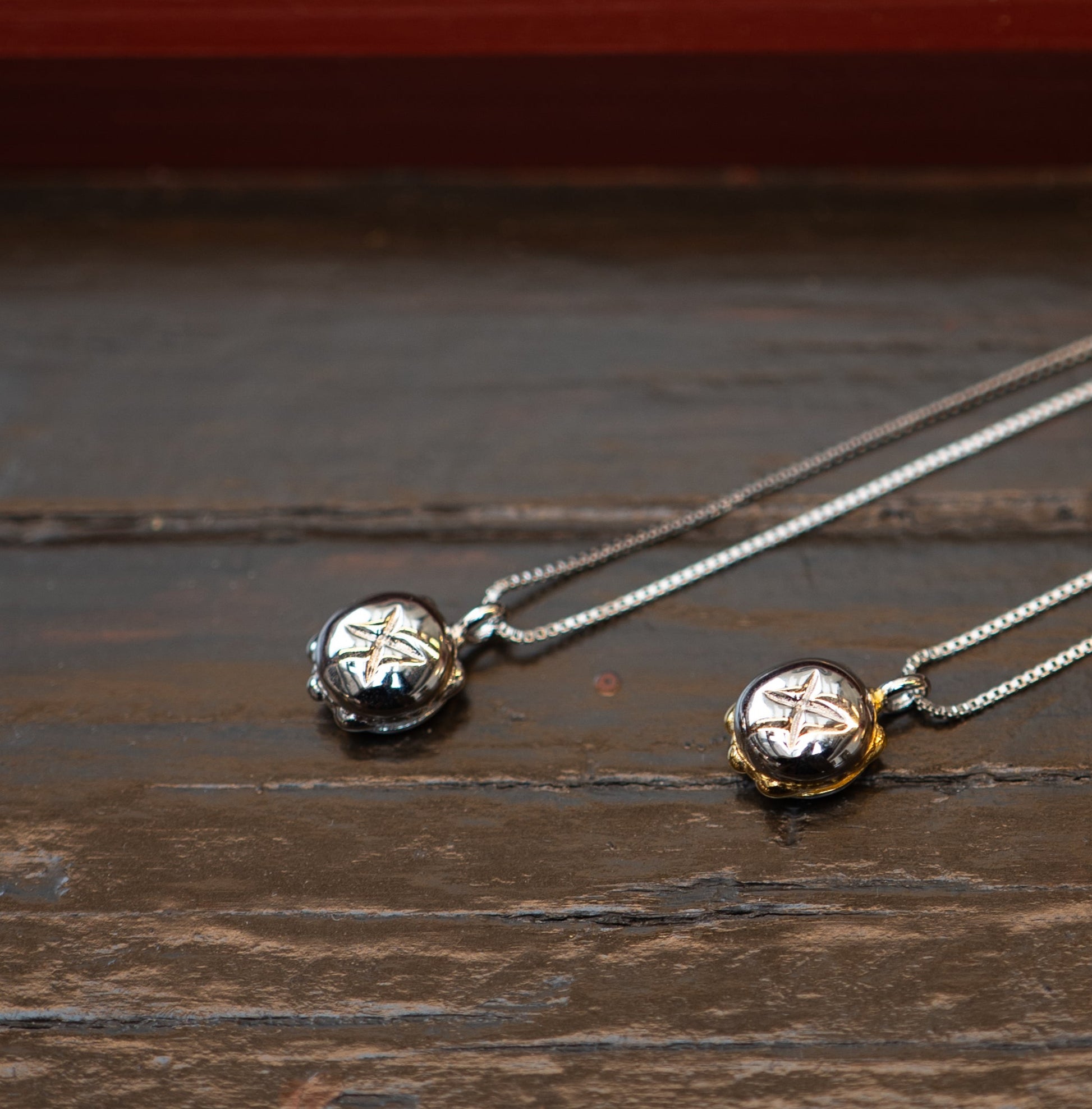 Zwei filigrane Ketten mit runden Anhängern liegen auf einer dunklen Holzoberfläche. Die Anhänger sind in Form eines kleinen Brötchens gestaltet, mit einer detaillierten Prägung auf der Oberfläche. Einer der Anhänger ist vollständig aus Sterling-Silber (925), während der andere mit einer hochwertigen Vergoldung veredelt ist. Die feinen Gliederketten unterstreichen das elegante Design des Schmuckstücks.