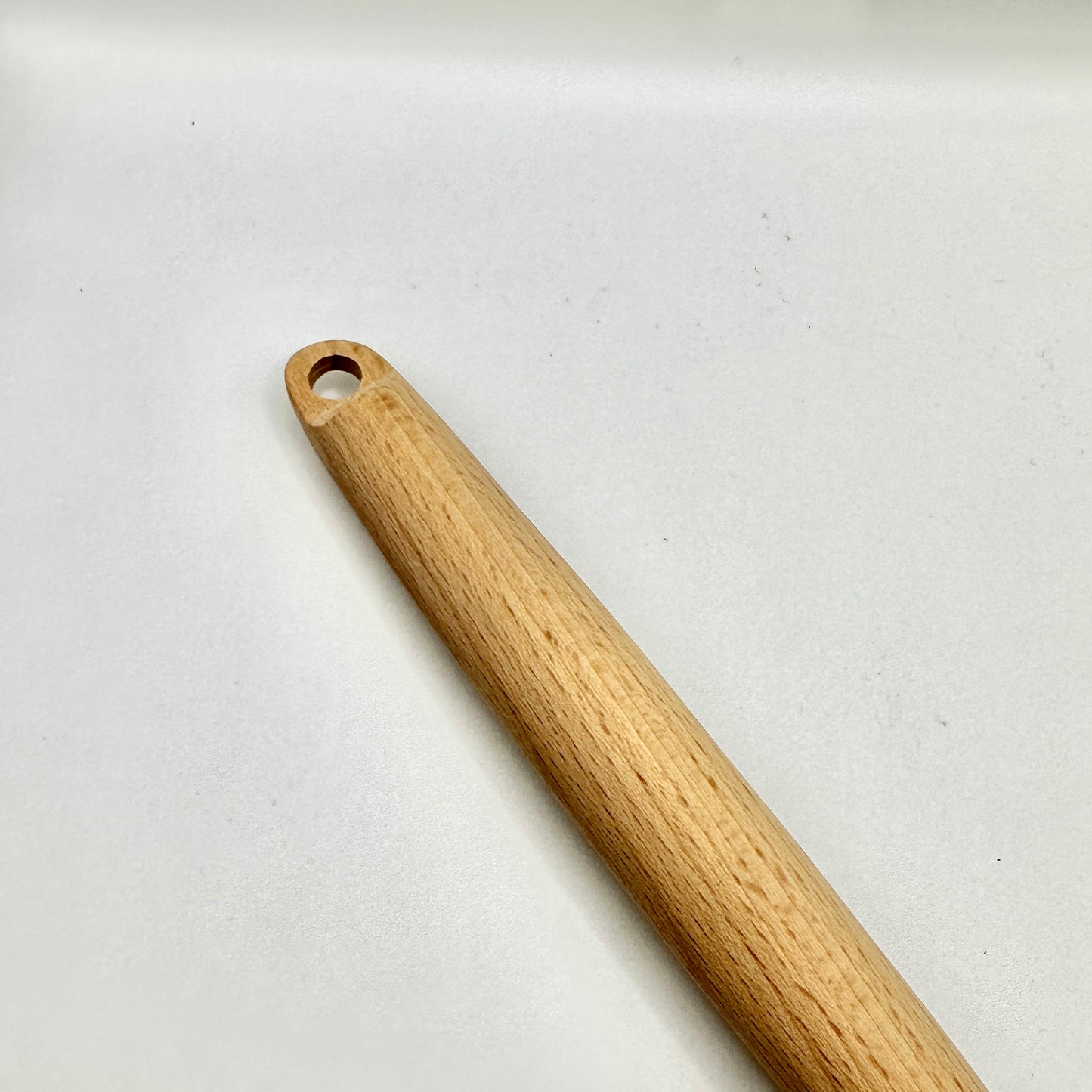Detailaufnahme des oberen Endes eines Holz-Kochlöffels mit einer praktischen Bohrung zum Aufhängen. Die glatte Oberfläche und die natürliche Holzstruktur verleihen dem Küchenutensil eine hochwertige Optik.