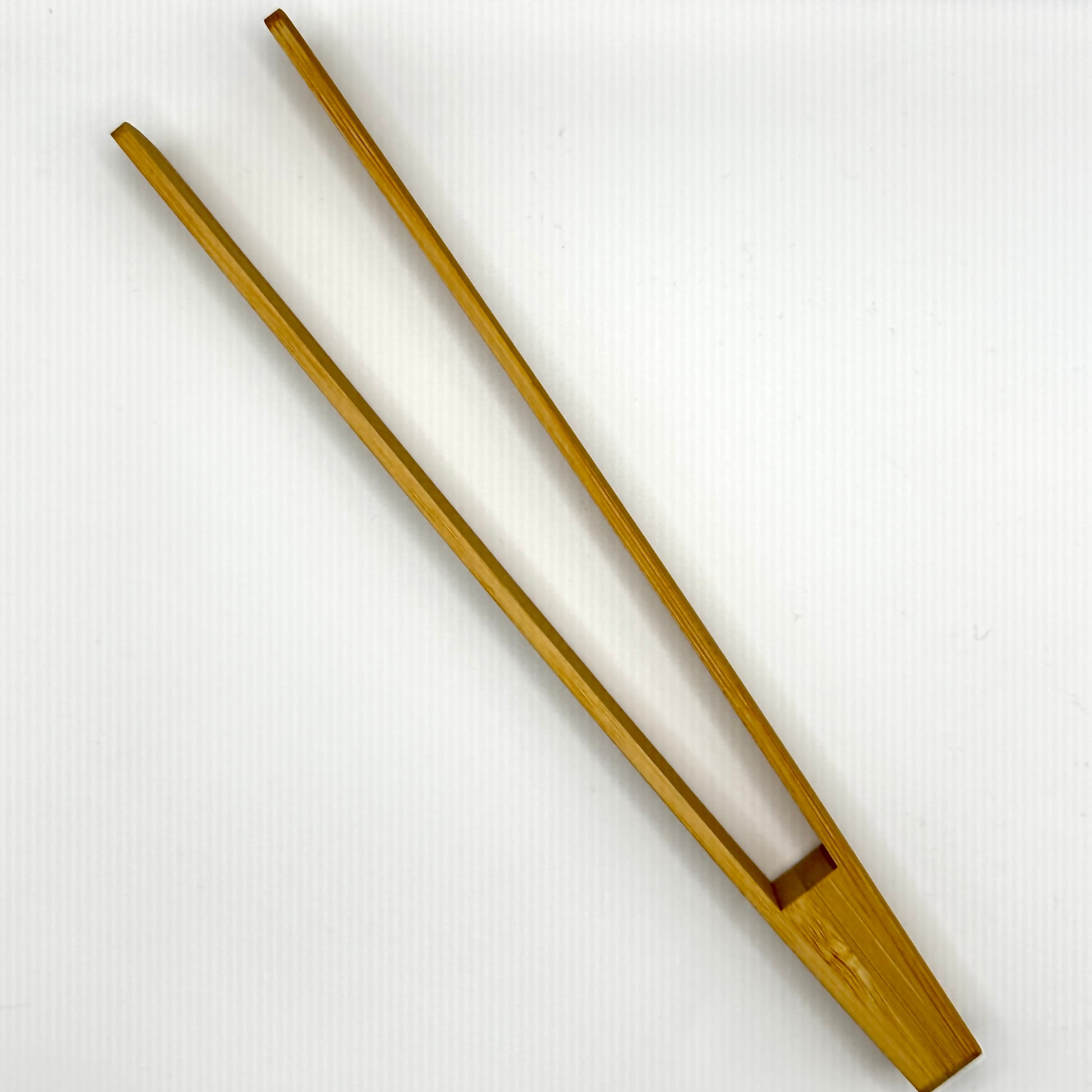 Eine geöffnete Holzzange, die zeigt, wie sie funktioniert. Die lange, schmale Form und die feine Verarbeitung machen sie ideal für den Einsatz in der Küche oder beim Servieren.