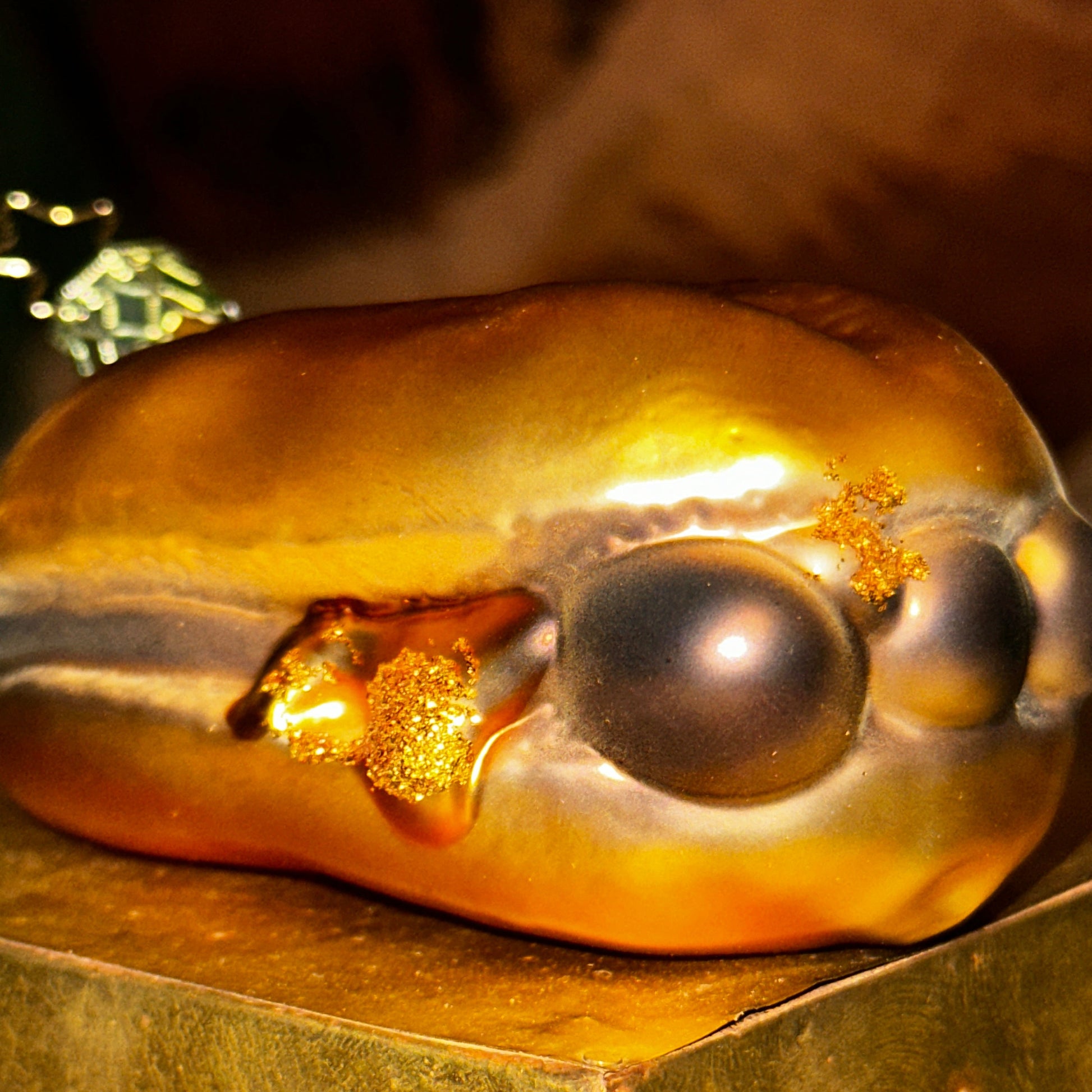 Nahaufnahme eines mundgeblasenen Christbaumschmucks in Form von "3 im Weggla". Die glänzende Glasfigur zeigt drei detailreich gestaltete Nürnberger Bratwürste in einem goldfarbenen Brötchen, mit feinen Glitzerelementen, die Senf oder Bratensaft symbolisieren. Die weichen Farbübergänge und die glänzende Oberfläche verleihen dem Ornament eine realistische und zugleich edle Optik. Der Christbaumschmuck liegt auf einem goldenen Podest.