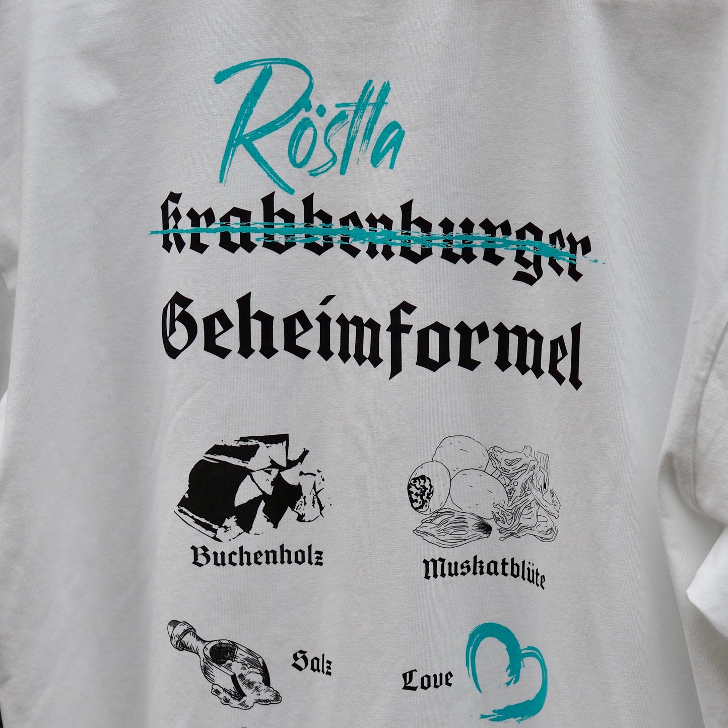 Weißes T-Shirt mit kreativem Design. Der Schriftzug „Krabbenburger“ ist durchgestrichen, darüber steht in türkis „Röstla“. Darunter ist in schwarzer gotischer Schrift „Geheimformel“ zu lesen. Ergänzt wird das Design durch Illustrationen und Begriffe wie „Buchenholz“, „Muskatblüte“, „Salz“ und „Love“, die in Verbindung mit der traditionellen Zubereitung von Röstla stehen. Ein humorvolles und stilvolles Statement-Shirt für Bratwurstliebhaber.
