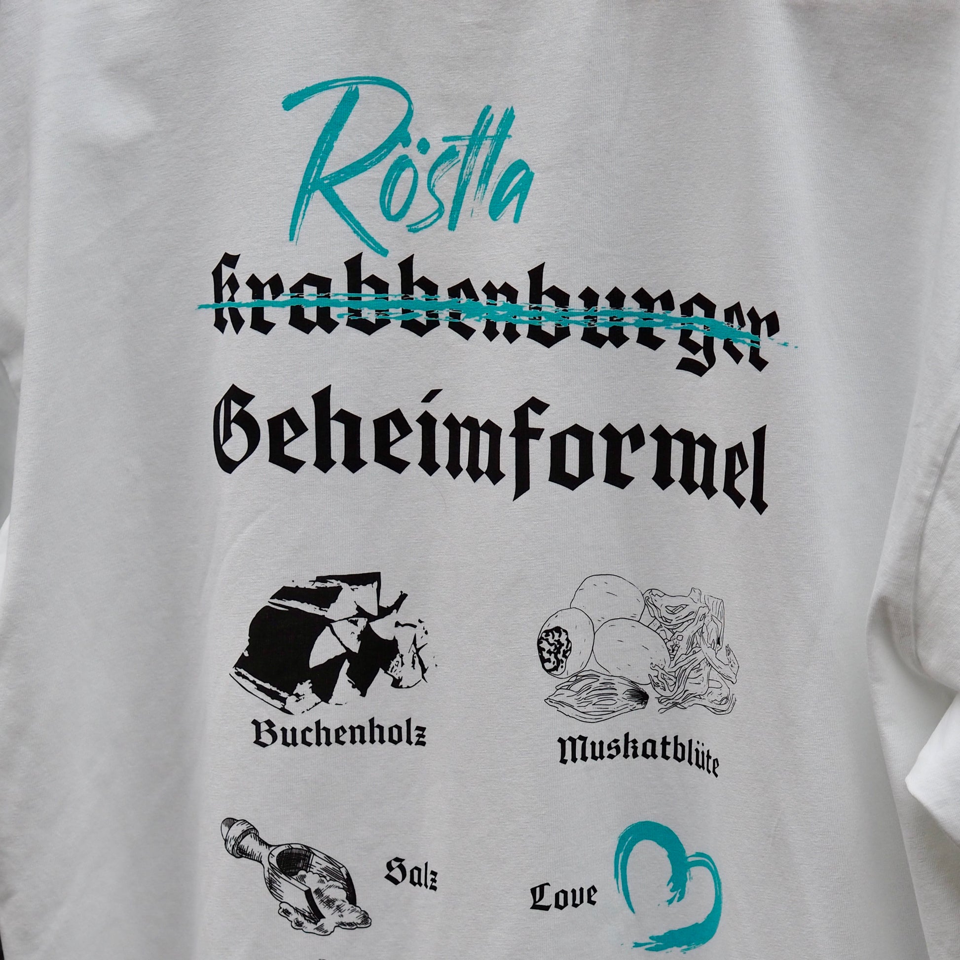 Weißes T-Shirt mit kreativem Design. Der Schriftzug „Krabbenburger“ ist durchgestrichen, darüber steht in türkis „Röstla“. Darunter ist in schwarzer gotischer Schrift „Geheimformel“ zu lesen. Ergänzt wird das Design durch Illustrationen und Begriffe wie „Buchenholz“, „Muskatblüte“, „Salz“ und „Love“, die in Verbindung mit der traditionellen Zubereitung von Röstla stehen. Ein humorvolles und stilvolles Statement-Shirt für Bratwurstliebhaber.