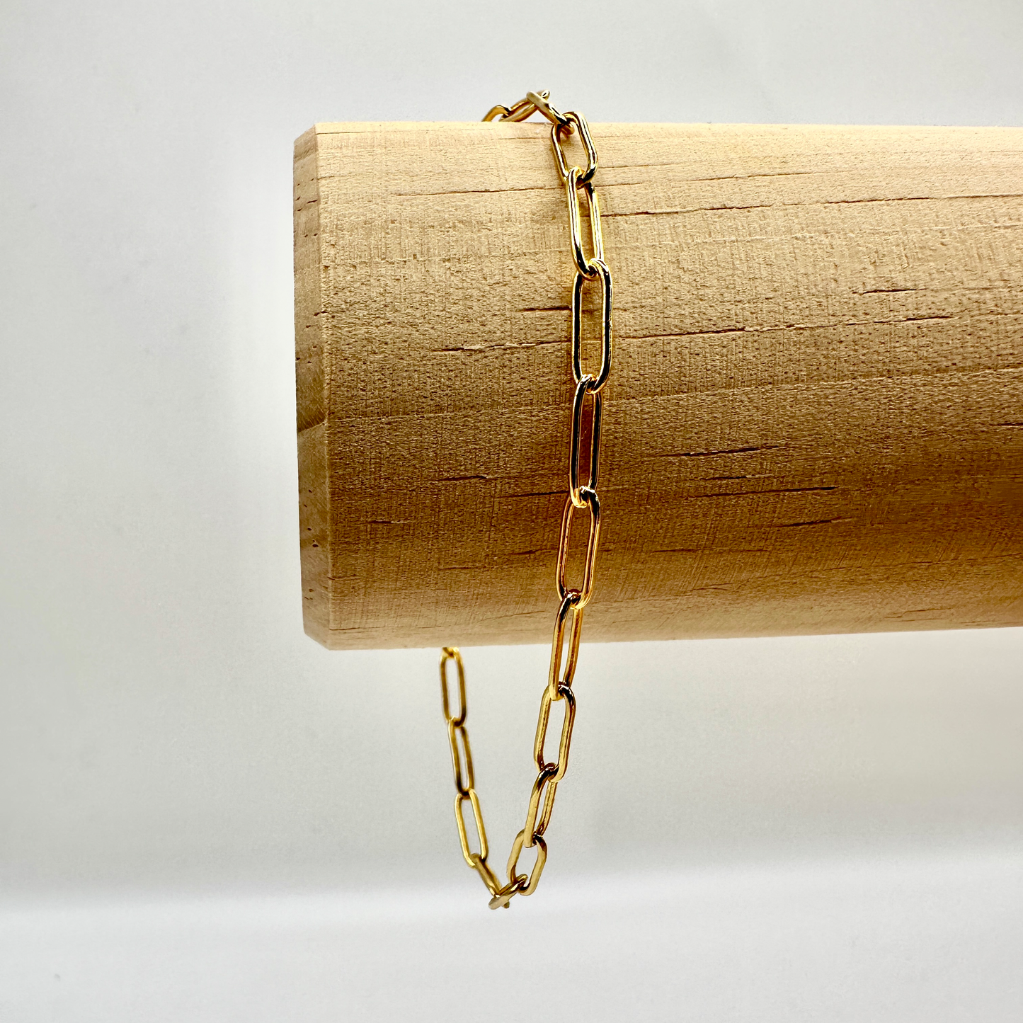 Elegantes Sammelarmband aus vergoldetem Sterling-Silber mit moderner Gliederkette. Die groben, rechteckigen Glieder verleihen dem Armband einen stilvollen und zeitlosen Look. Präsentiert auf einer hölzernen Stange, die die hochwertige Verarbeitung und den edlen Glanz des Schmucks hervorhebt. Ideal zum Kombinieren mit individuellen Anhängern.