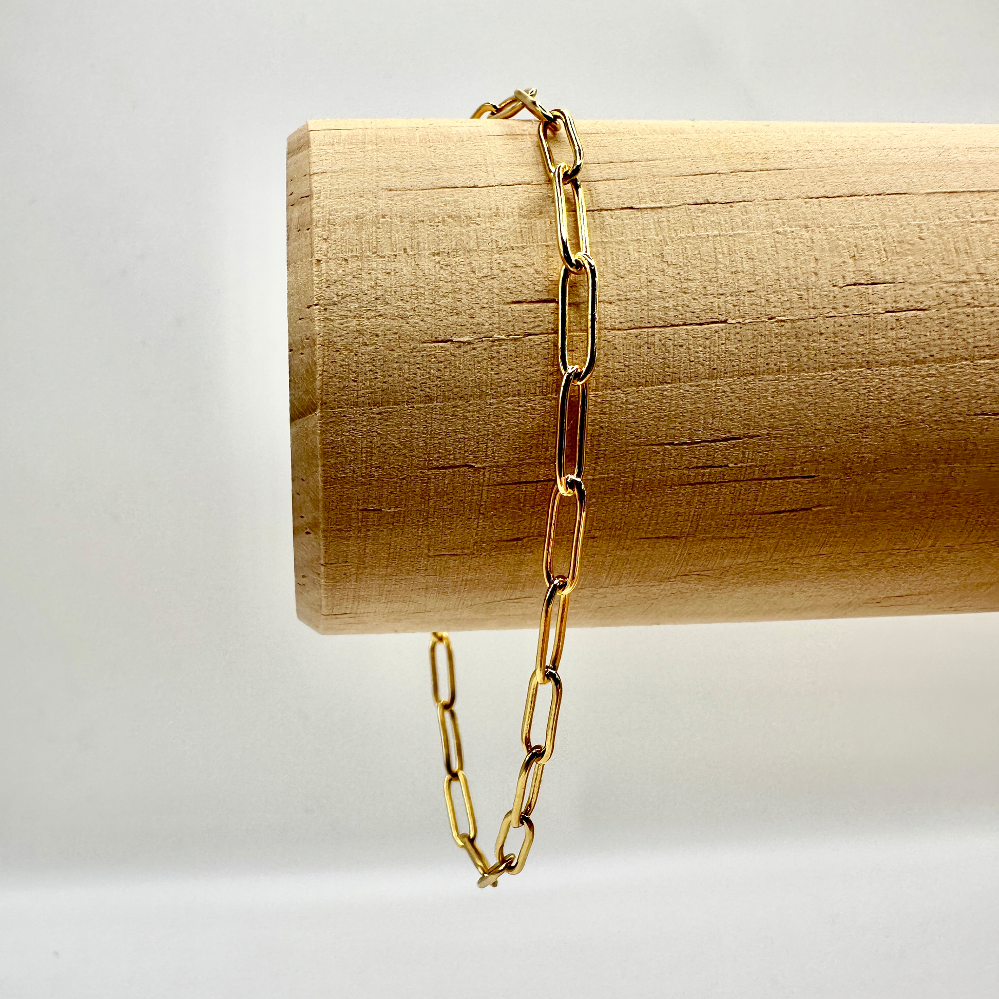 Elegantes Sammelarmband aus vergoldetem Sterling-Silber mit moderner Gliederkette. Die groben, rechteckigen Glieder verleihen dem Armband einen stilvollen und zeitlosen Look. Präsentiert auf einer hölzernen Stange, die die hochwertige Verarbeitung und den edlen Glanz des Schmucks hervorhebt. Ideal zum Kombinieren mit individuellen Anhängern.