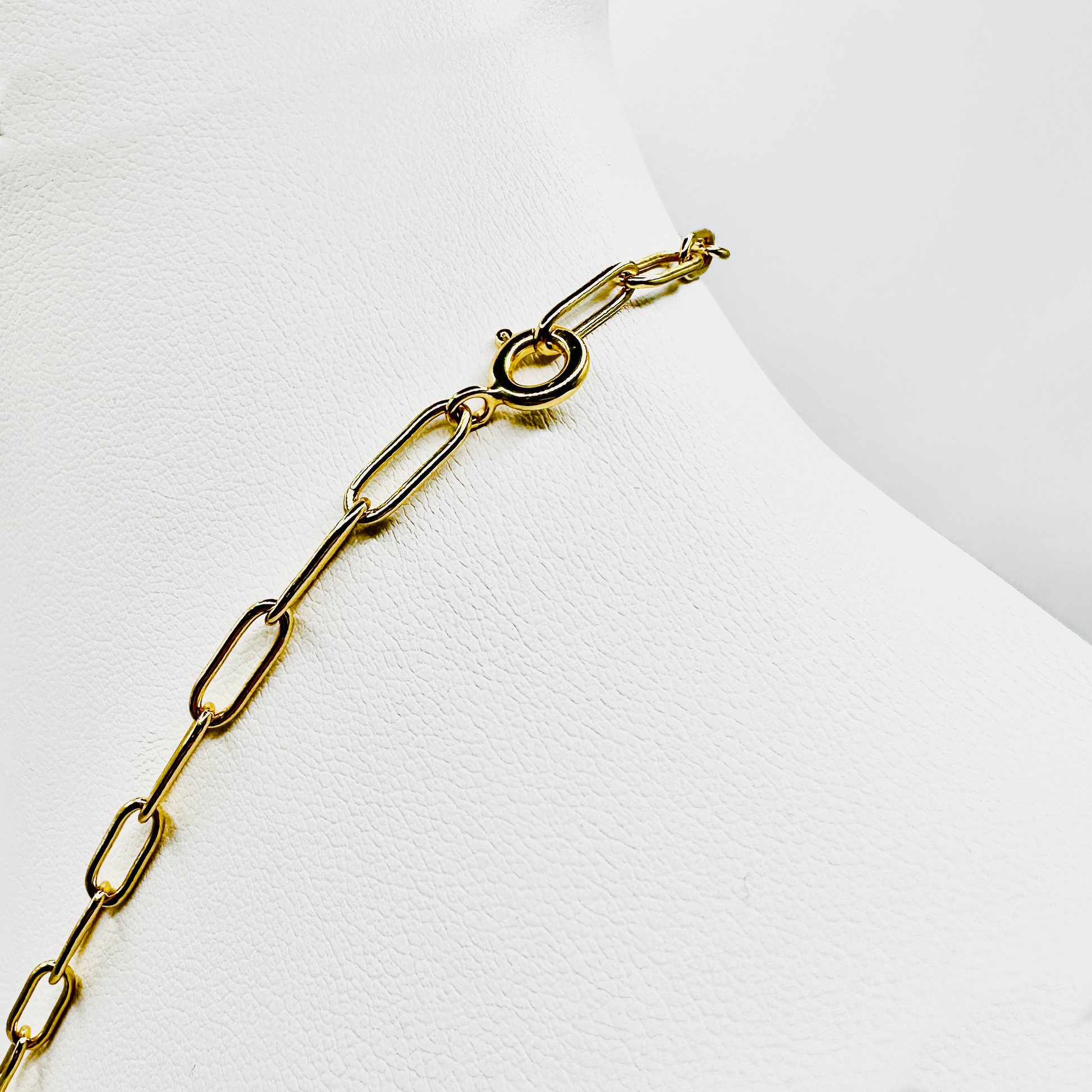 Nahaufnahme des Verschlusses einer goldenen Gliederkette, präsentiert auf einem weißen Schmuckdisplay. Die Kette besteht aus rechteckigen, filigranen Gliedern mit einer hochwertigen 3 Micron Vergoldung auf Sterling Silber (925). Der Verschluss ist ein klassischer Federring, der sich sicher und einfach schließen lässt. Das elegante Design macht die Kette zur idealen Basis für das Sammeln und Tragen von Anhängern.