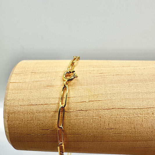 Detailaufnahme eines eleganten Sammelarmbands aus vergoldetem Sterling-Silber, präsentiert auf einer hölzernen Stange. Der stabile Federringverschluss sorgt für sicheren Halt, während die filigrane Gliederkette eine stilvolle Basis für individuelle Anhänger bietet. Hochwertige Verarbeitung und zeitloses Design für vielseitige Schmuckkombinationen.