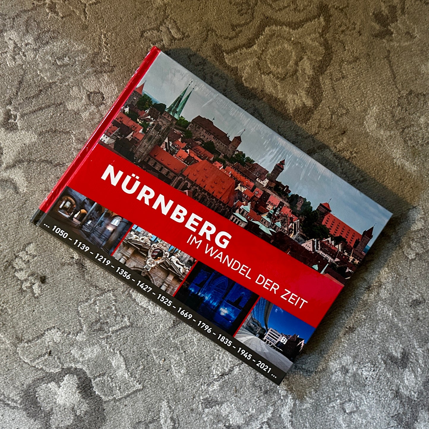 Vorderseite des Buches Nürnberg im Wandel der Zeit mit einem großflächigen Stadtbild und kleineren Bildern, die verschiedene architektonische Epochen zeigen. Der Titel ist in markantem Rot hervorgehoben.