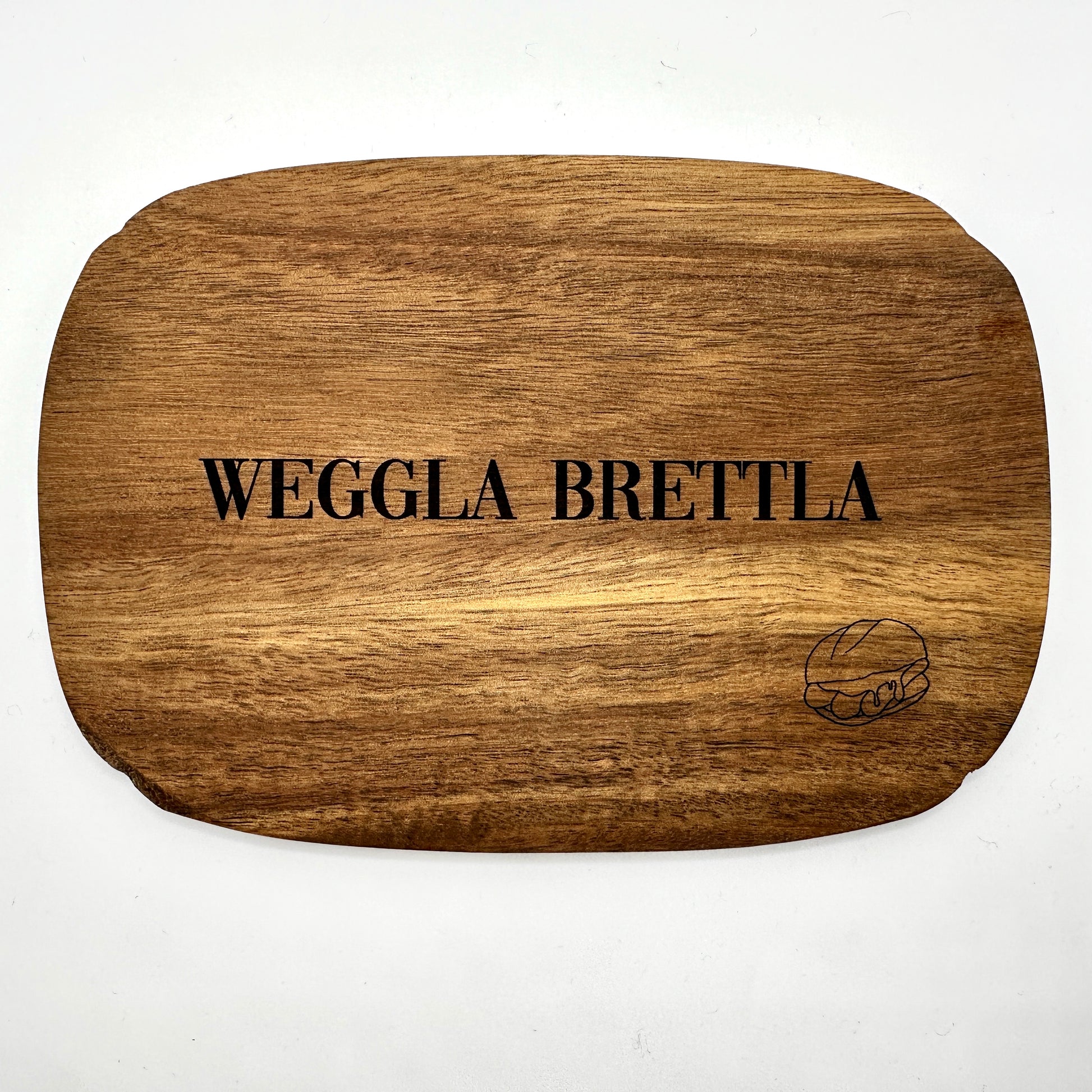 Ein hochwertiges Schneidebrett aus Holz mit der Gravur „Weggla Brettla“ in schwarzer Schrift. In der unteren rechten Ecke ist eine feine Gravur eines Brötchens mit drei Bratwürsten zu sehen. Das Brett hat eine abgerundete Form und eine warme Holzmaserung, die dem Design eine rustikale und authentische Note verleiht. Perfekt als Servierbrett oder stilvolles Küchenaccessoire für Liebhaber fränkischer Spezialitäten.