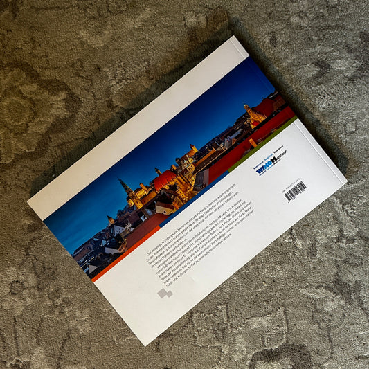Die Rückseite eines Buches mit dem Titel „In Nürnberg“. Das Cover zeigt eine beeindruckende Panoramaaufnahme der Nürnberger Altstadt bei Nacht mit stimmungsvoller Beleuchtung. Im unteren Bereich befindet sich eine Beschreibung des Buchinhalts, begleitet vom Logo des Verlags.
