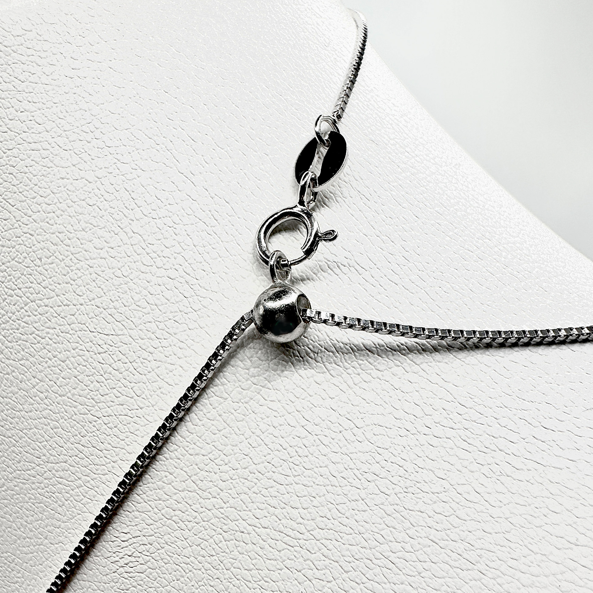 Nahaufnahme eines silbernen Kettenverschlusses mit einer verstellbaren Kugelmechanik. Die feine Kette besitzt einen klassischen Federringverschluss, der an einer kleinen ovalen Plakette befestigt ist. Die glänzende Oberfläche und die hochwertige Verarbeitung unterstreichen die Eleganz und Funktionalität des Designs. Die Kugel ermöglicht eine flexible Längenanpassung für optimalen Tragekomfort.