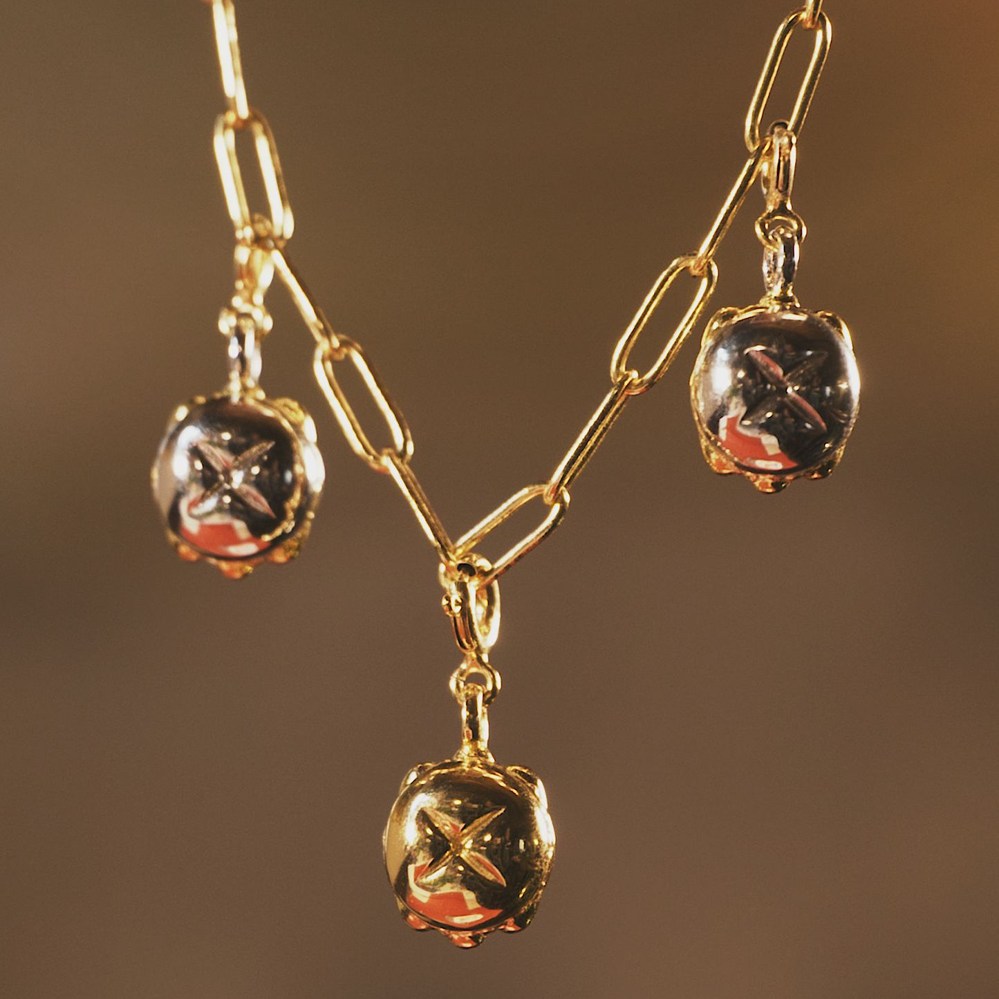 Detailaufnahme einer goldenen Sammelkette mit drei glänzenden Anhängern in Form des traditionellen „Drei im Weggla“. Die Anhänger bestehen aus einer Kombination aus Gold und Silber und sind an einer feinen, länglichen Gliederkette befestigt. Der Schmuck reflektiert das warme Licht und unterstreicht die edle Verarbeitung der Anhänger.