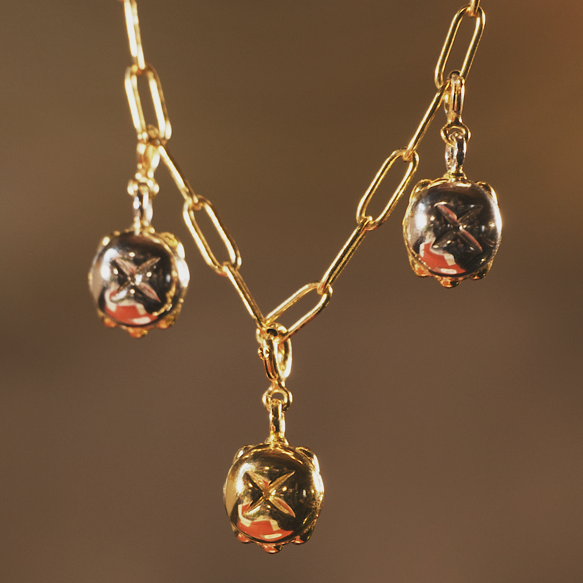 Detailaufnahme einer goldenen Sammelkette mit drei glänzenden Anhängern in Form des traditionellen „Drei im Weggla“. Die Anhänger bestehen aus einer Kombination aus Gold und Silber und sind an einer feinen, länglichen Gliederkette befestigt. Der Schmuck reflektiert das warme Licht und unterstreicht die edle Verarbeitung der Anhänger.