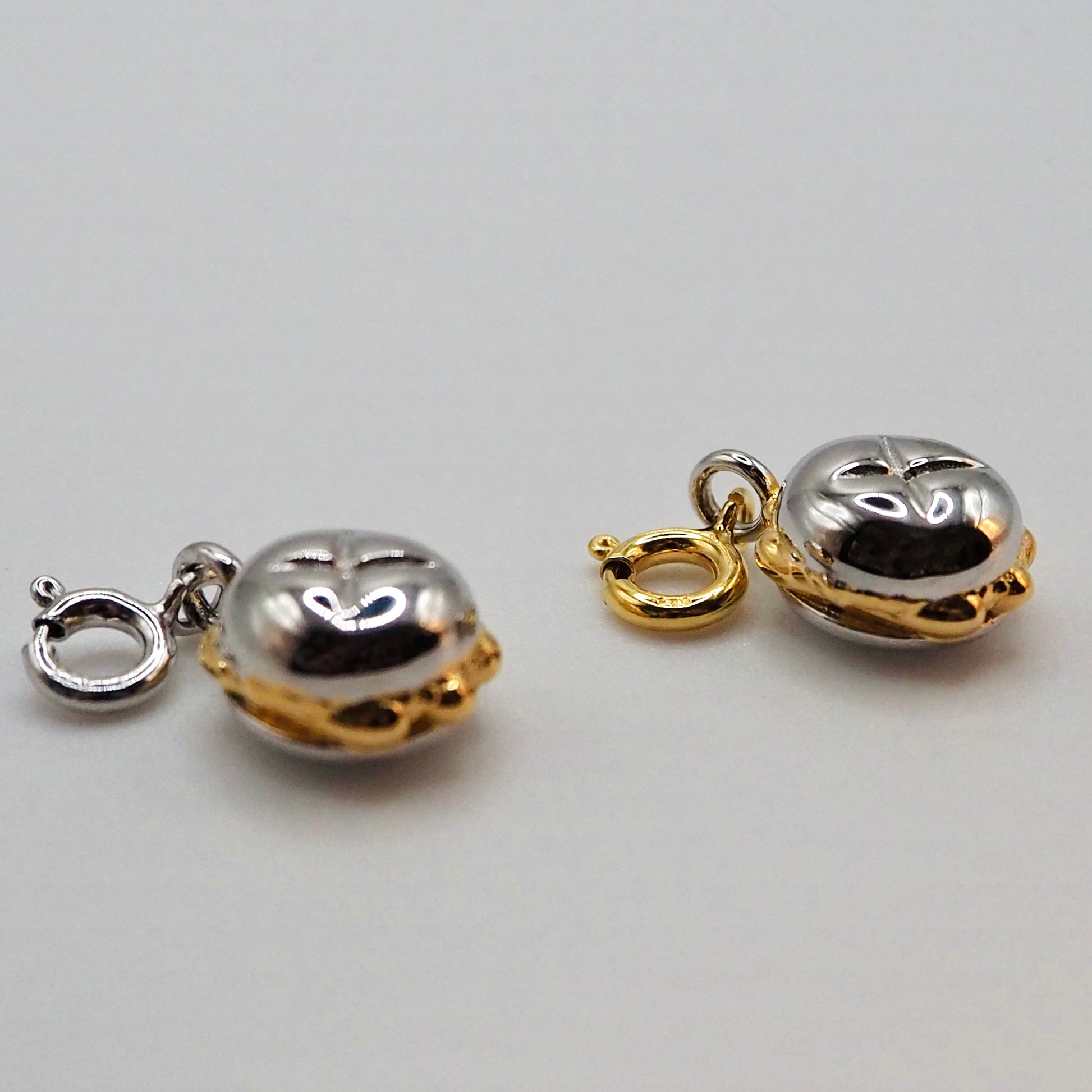 Nahaufnahme von zwei kleinen „3 im Weggla“ Charms aus Sterling-Silber mit vergoldeten Akzenten. Die Charms haben eine detaillierte Brötchenstruktur und sind mit einem Karabinerverschluss versehen. Perfekt für Armbänder oder Ketten.