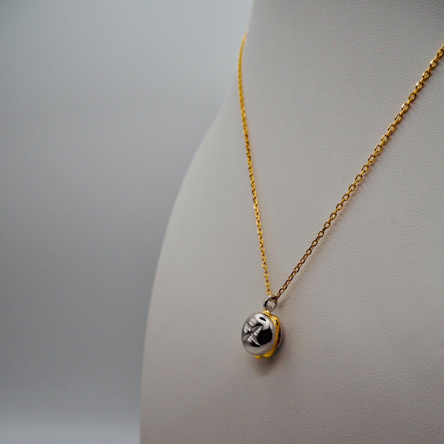 Eine elegante, vergoldete Kette mit einem detailreichen Bicolor-Anhänger in Form eines „3 im Weggla“ – präsentiert auf einem weißen Schmuckdisplay. Der glänzende Silberanhänger, umrandet von vergoldeten Akzenten, kombiniert Tradition mit edlem Design.