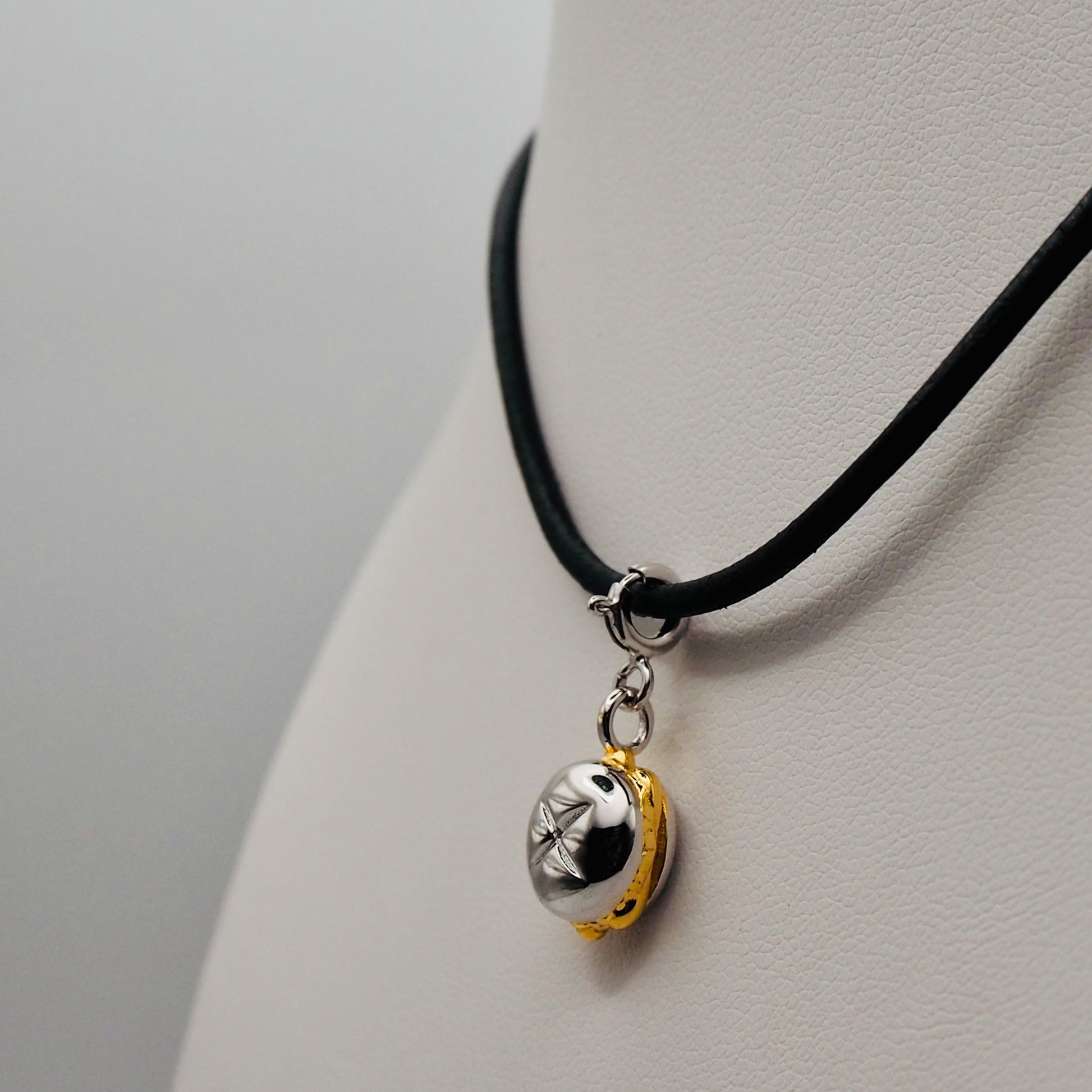 Ein außergewöhnlicher Anhänger in Form von drei goldenen Bratwürsten in einem silbernen Brötchen, hängend an einer schwarzen Lederkette, präsentiert auf einer weißen Schmuckbüste.