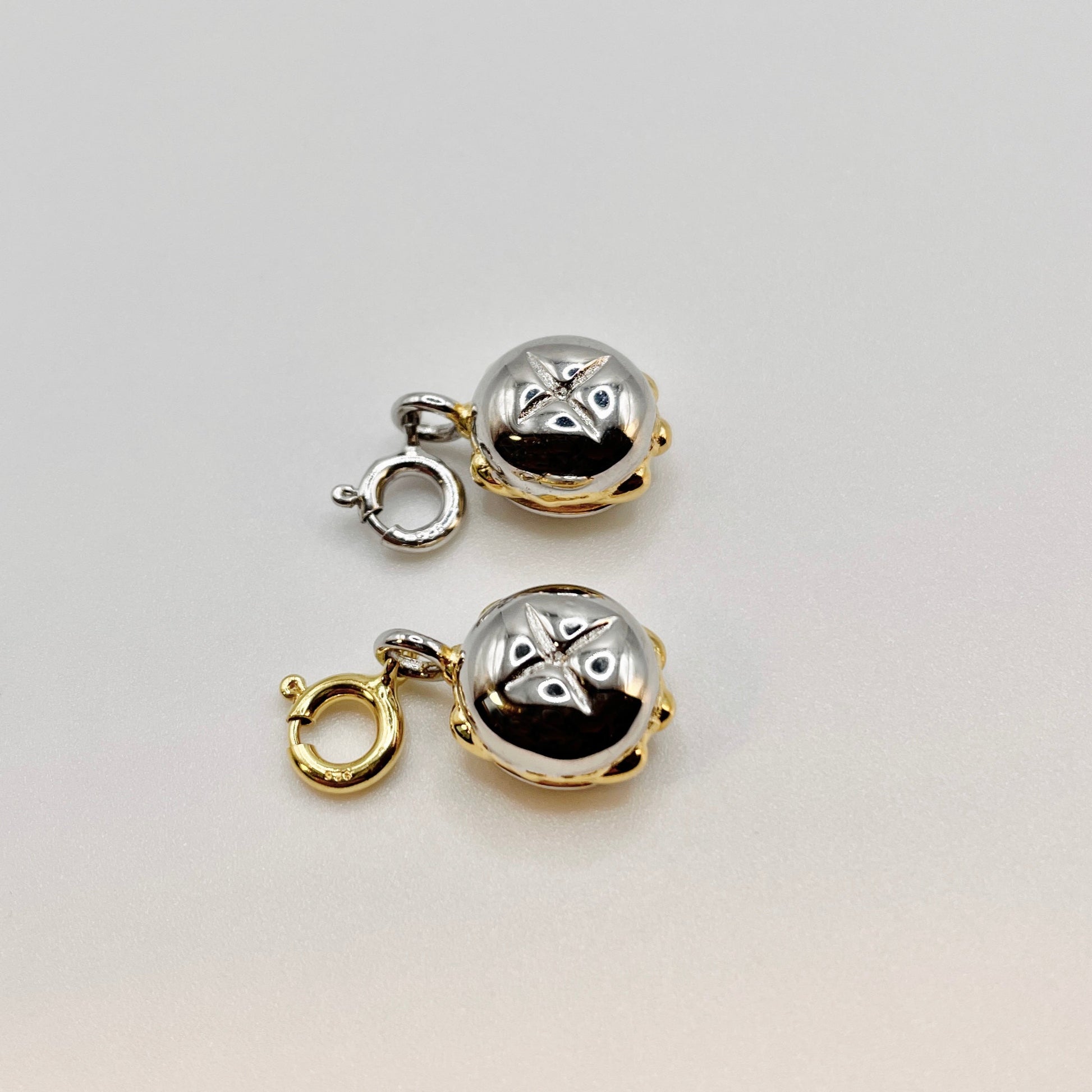 Zwei hochwertige Charms in Form eines kleinen runden Brötchens mit eingeschnittener Kruste, gefertigt aus glänzendem Sterling-Silber mit vergoldeten Akzenten. Beide Charms sind mit einem praktischen Karabinerverschluss versehen – einer in Silber, der andere in Gold – und eignen sich perfekt zur Befestigung an Armbändern oder Ketten. Elegantes Schmuckdesign inspiriert von der fränkischen Genusskultur.