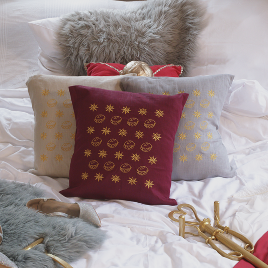 Drei dekorative Leinenkissen in den Farben Mondgrau, Sandstein und Weinrot mit goldener Stickerei, die eine Musterung aus kleinen Brötchen („Weggla“) und Sternen („Sternla“) zeigt. Die Kissen sind inklusive Füllung und liegen auf einem stilvoll arrangierten Bett mit weiteren Dekoelementen wie einem grauen Kunstfell-Kissen, einem roten Samtkissen mit goldenen Details, einem silberne Schuh und einer goldenem Zepter.