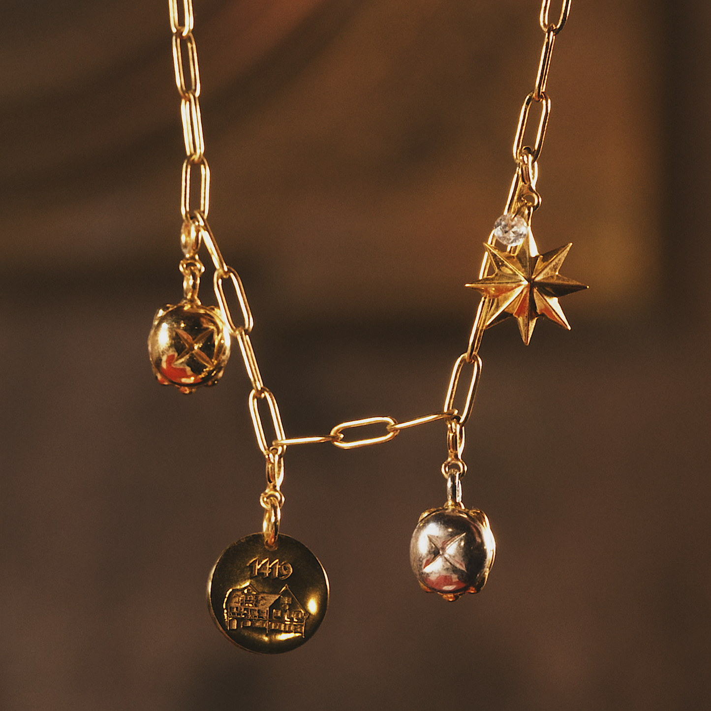 Elegante goldene Sammelkette mit drei detailreich gestalteten Anhängern: Ein runder Medaillon-Anhänger mit der Gravur "1419" und der historischen Bratwurstküche, ein glänzender Stern mit facettierten Kanten sowie zwei Miniatur-Nachbildungen des berühmten Nürnberger „3 im Weggla“. Die Kette besticht durch ihre filigranen Glieder und die warmen Goldtöne, die in sanftem Licht erstrahlen. Ein edles Schmuckstück mit historischem Charme.