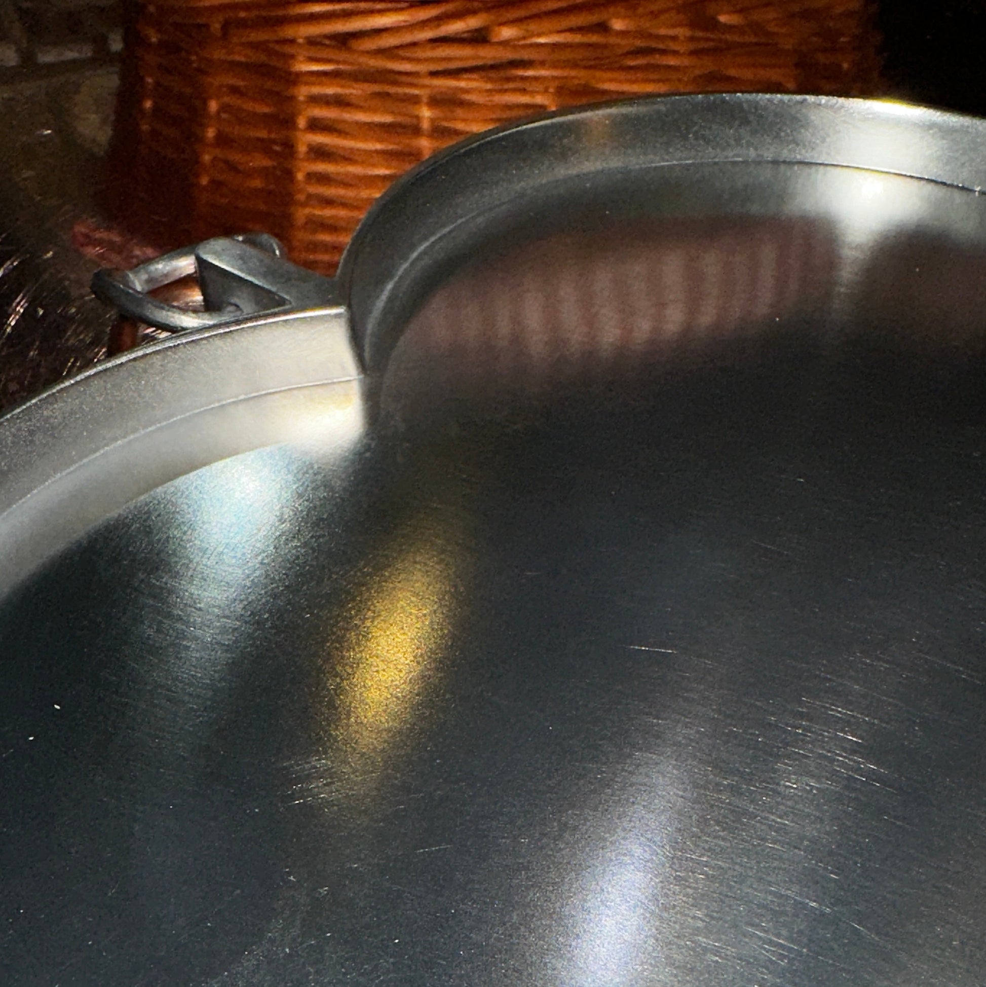 Nahaufnahme eines herzförmigen Zinntellers mit gebürsteter, matt glänzender Oberfläche. Lichtreflexe betonen die feine Struktur des Metalls, während der leicht erhöhte Rand und der integrierte Metall-Aufhänger in Ringform sichtbar sind. Der Hintergrund ist verschwommen, mit warmen Farbtönen, die sich sanft auf der reflektierenden Oberfläche spiegeln.