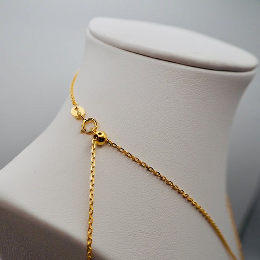 Nahaufnahme des Verschlusses einer eleganten, vergoldeten Kette, präsentiert auf einem weißen Schmuckdisplay. Die feingliedrige Kette verfügt über einen hochwertigen Karabinerverschluss und eine verstellbare Perle zur individuellen Längenanpassung. Ein kleines, rundes Plättchen am Verschluss sorgt für eine edle Detailveredelung.