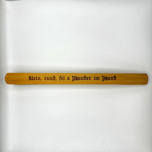 Eine hochwertige Holzzange mit der Gravur „klein, rund, sei a Wunder im Mund“ in traditioneller Frakturschrift. Die Zange ist aus natürlichem Holz gefertigt und überzeugt durch ihre schlichte, elegante Form.
